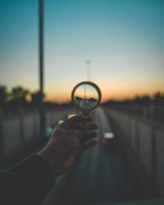 Hand holding magnifying glass at sunset signifying deep focus.